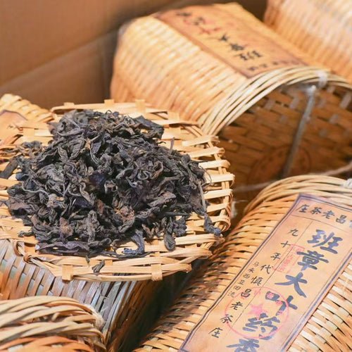 Dried black (raw pu-erh) tea leaves in a woven basket with wooden background