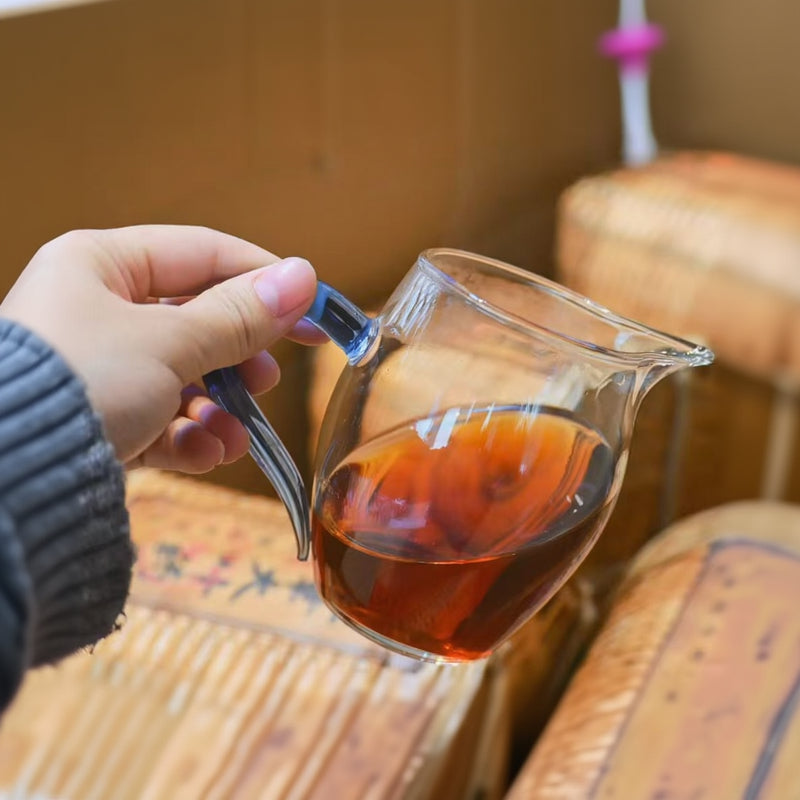 Hand holding a glass teapot with tea, blurred background