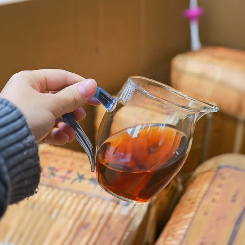 Hand holding a glass teapot with tea, blurred background