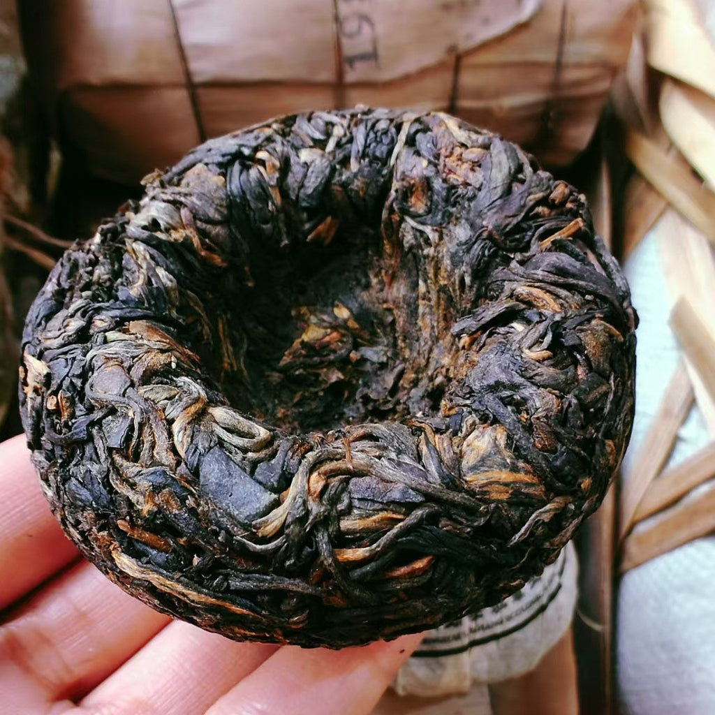 Round dark brown raw puerh tea cake held in a hand 