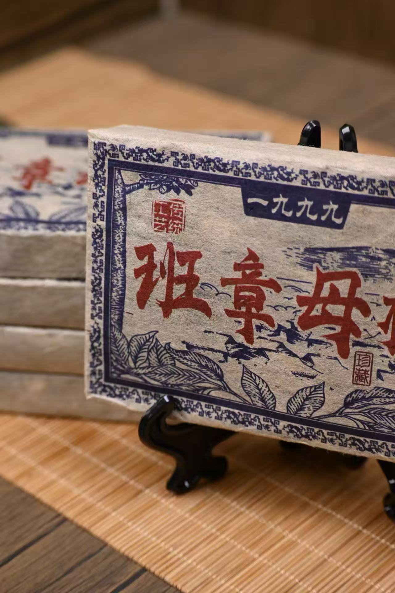 Traditional Chinese text on a stack of books with a wooden stand on a woven mat background compressed Ban Zhang pu-erh tea cake close up