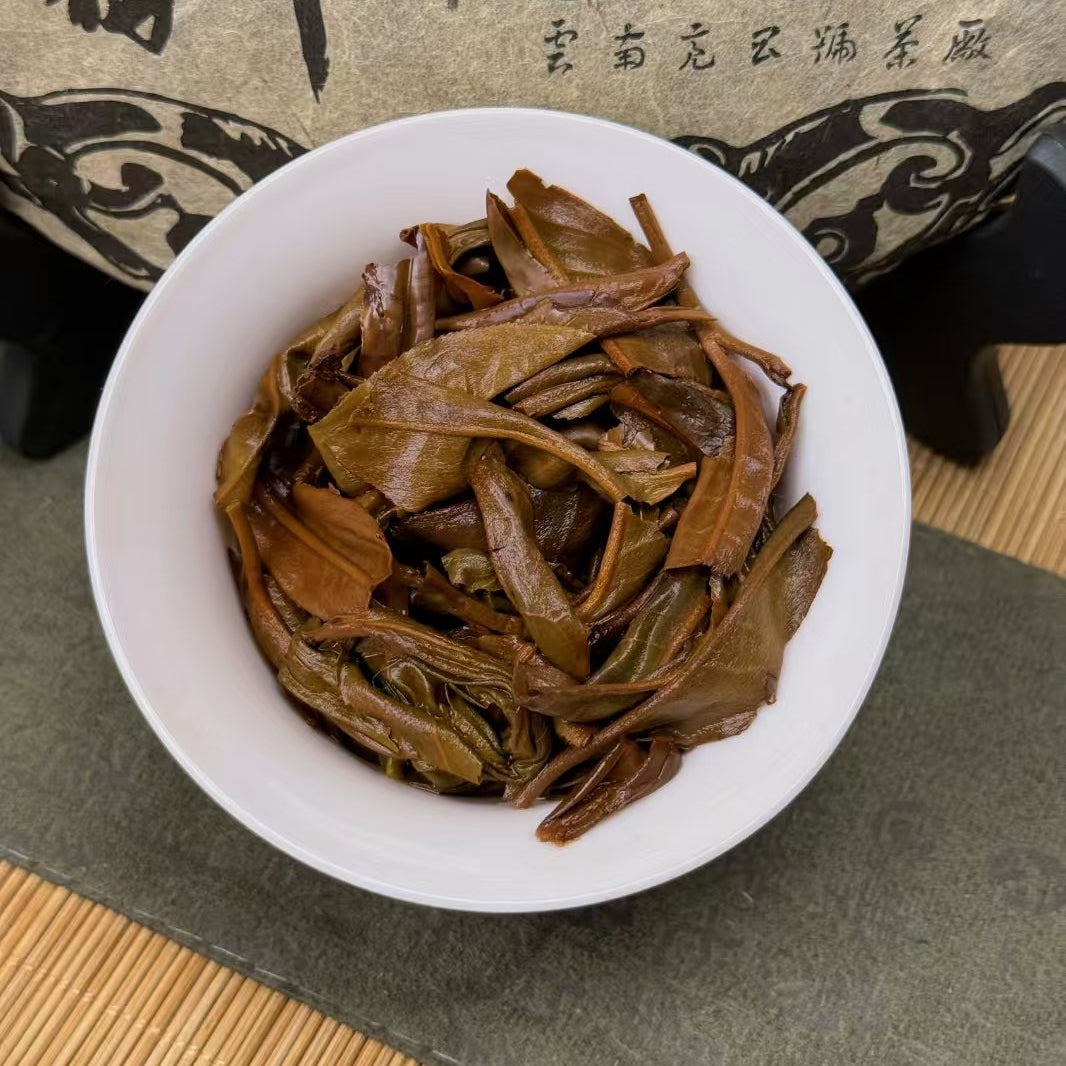 White bowl filled with green tea leaves on a textured surface with a tea box in the background.