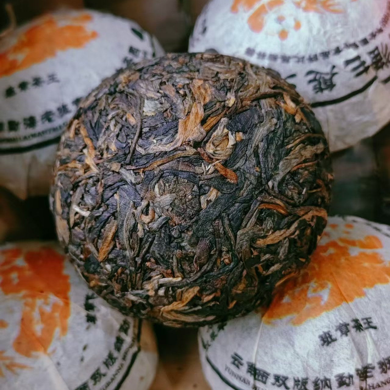 Close-up of a large raw pu-erh tea ball with smaller tea balls in the background