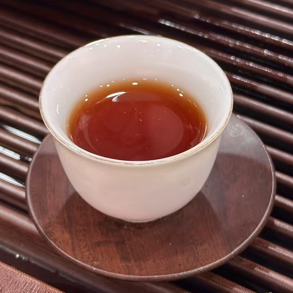 White ceramic cup rich brewed liquor of ripe pu-erh tea from Yunnan with dark liquid on a wooden surface